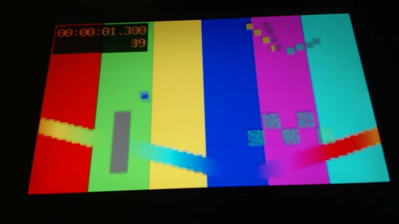 A monitor photographed in a dark room, showing a decoded video frame: six vertical colour bars in red, green, yellow, blue, magenta and cyan, crossed by diagonal stepped bands, with a timecode overlay reading 00:00:01.300 and a frame number 39.